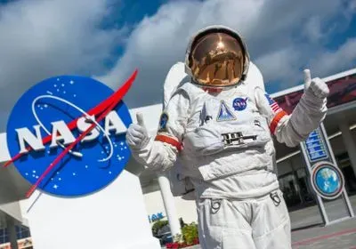 an astronaut gives two thumbs up next to a NASA sign